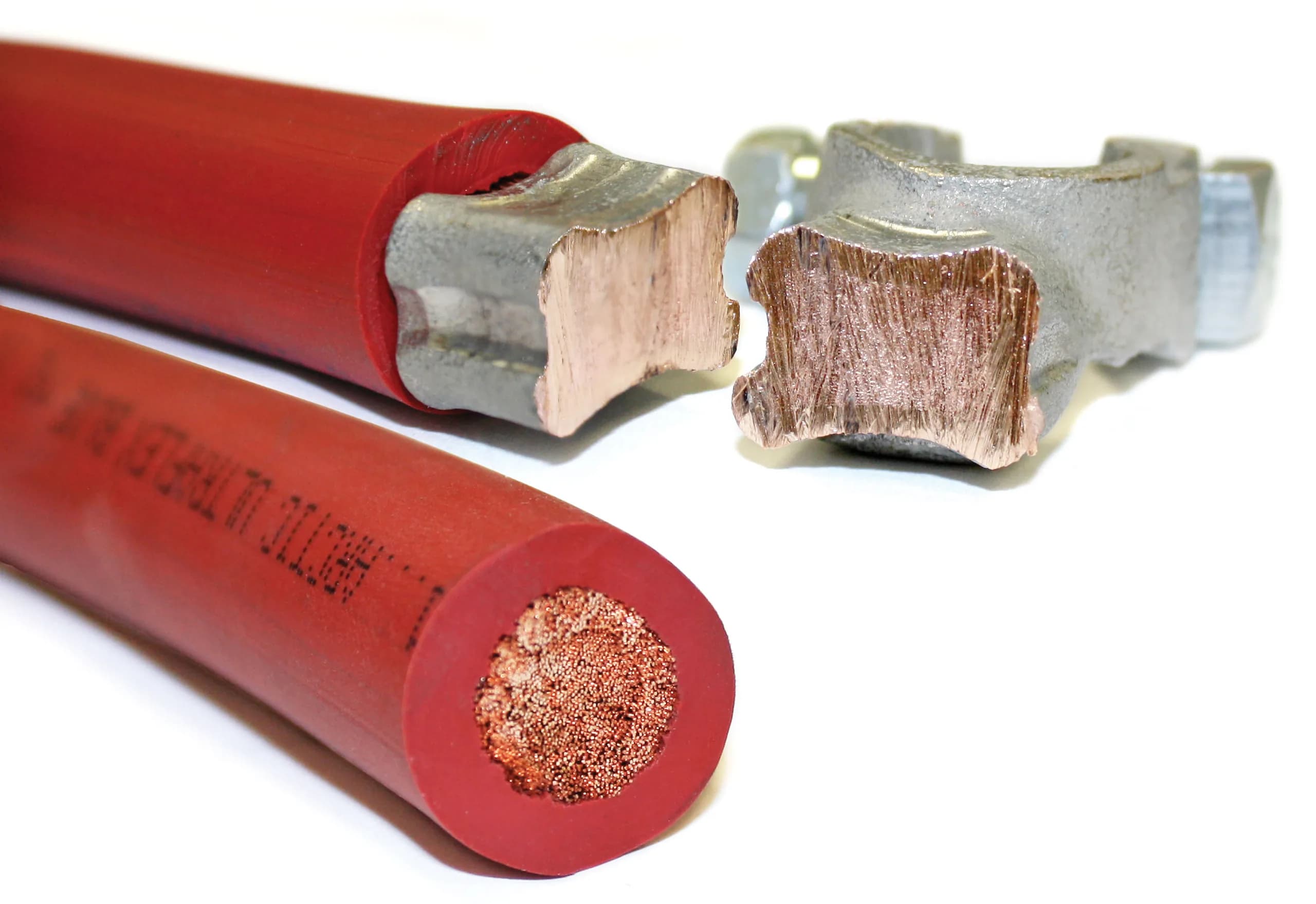 Red cable beside a sectioned compression lug, showing the crimped copper inside the barrel