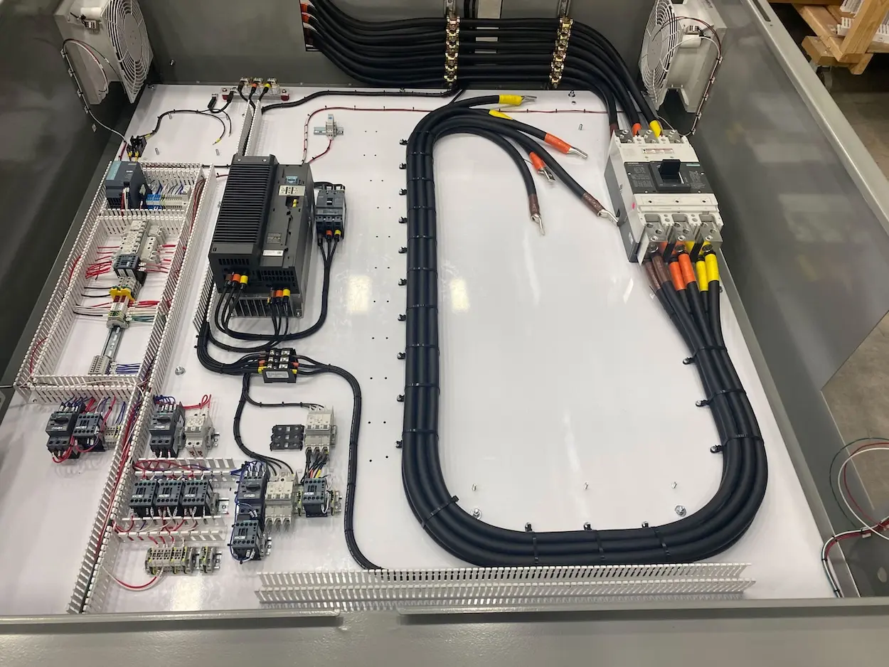A control cabinet with heavy black cable routed to breakers and terminals