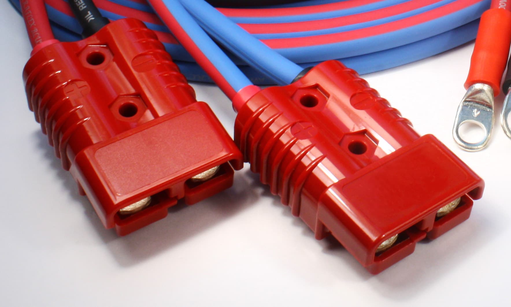 Two red Lexan power connectors on blue and red jumper cable, beside plated ring lugs