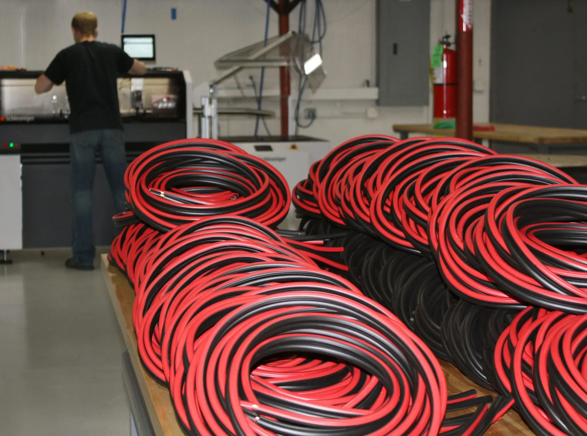 Red and black private label cable coiled on a bench, operator at a cutting machine